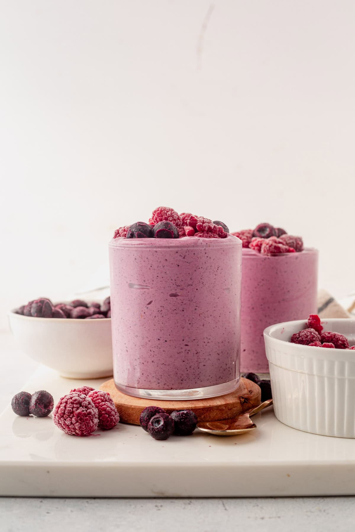 two raspberry blueberry smoothies on coasters surrounded by frozen berries.