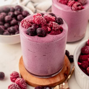 a blueberry raspberry smoothie on a coaster topped with frozen berries.