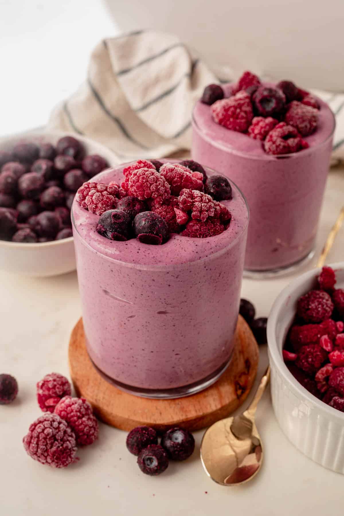 two blueberry raspberry smoothies on a countertop with fresh berries on top.