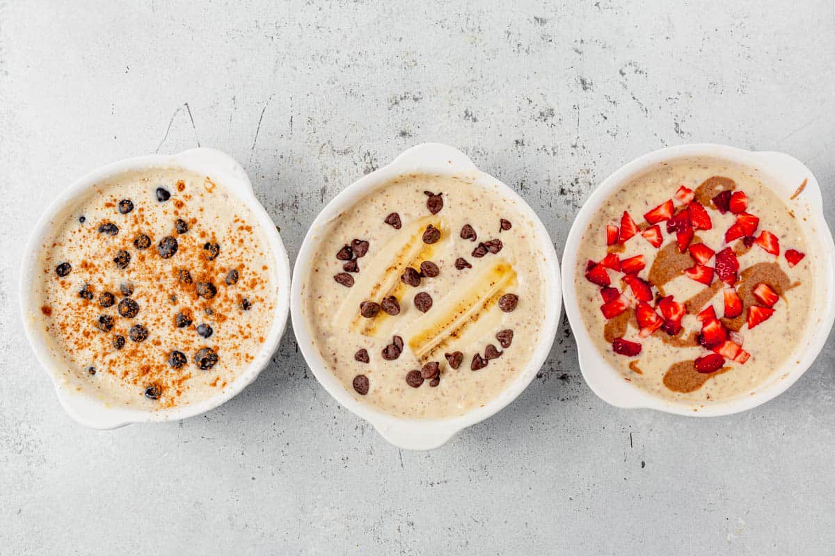 protein pancake batter in three separate bowls with fruit toppings.