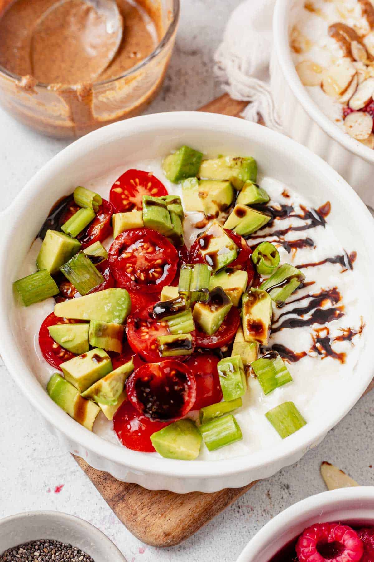 savory breakfast bowl with avocado, tomato, and green onions on a counter.