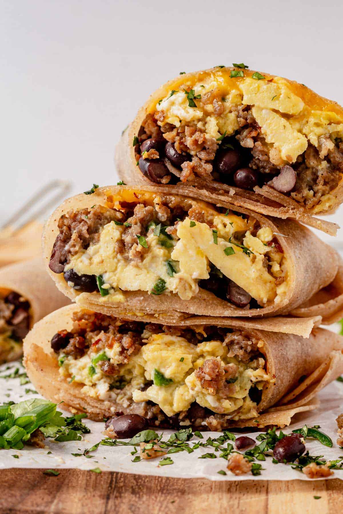 three high protein breakfast burritos stacked on a cutting board.