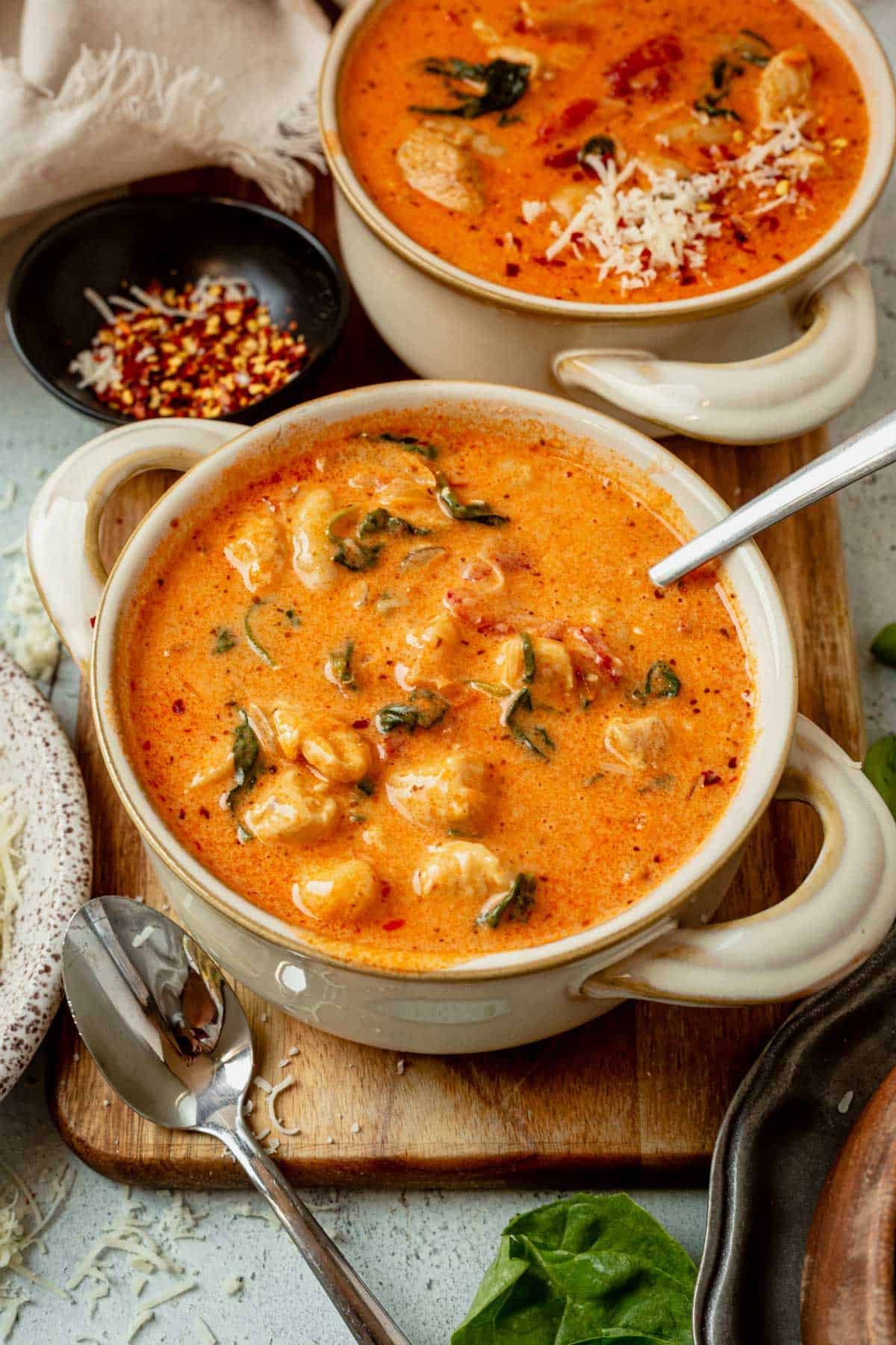 two bowls of marry me chicken soup on a serving board with fresh parmesan.