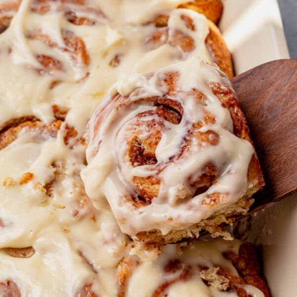 pulling a protein cinnamon roll out of the baking dish.