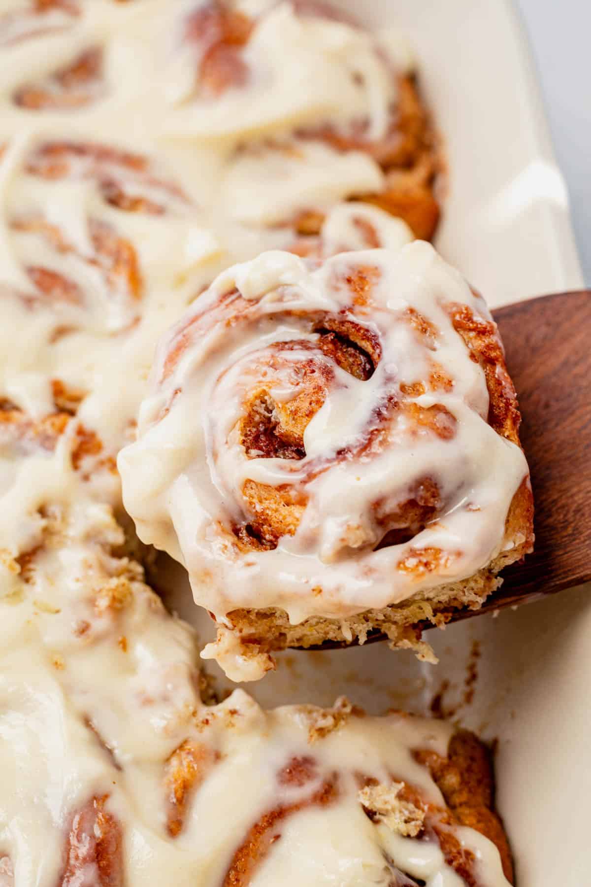 pulling a protein cinnamon roll with frosting out of the tray.