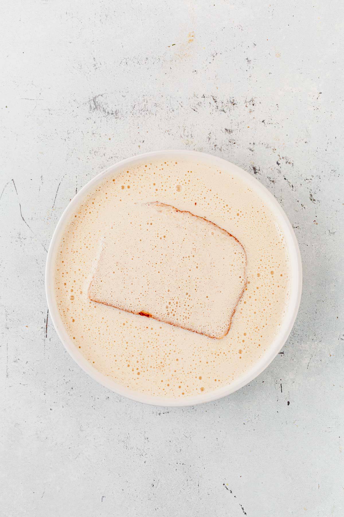 a piece of bread soaking in protein french toast batter.