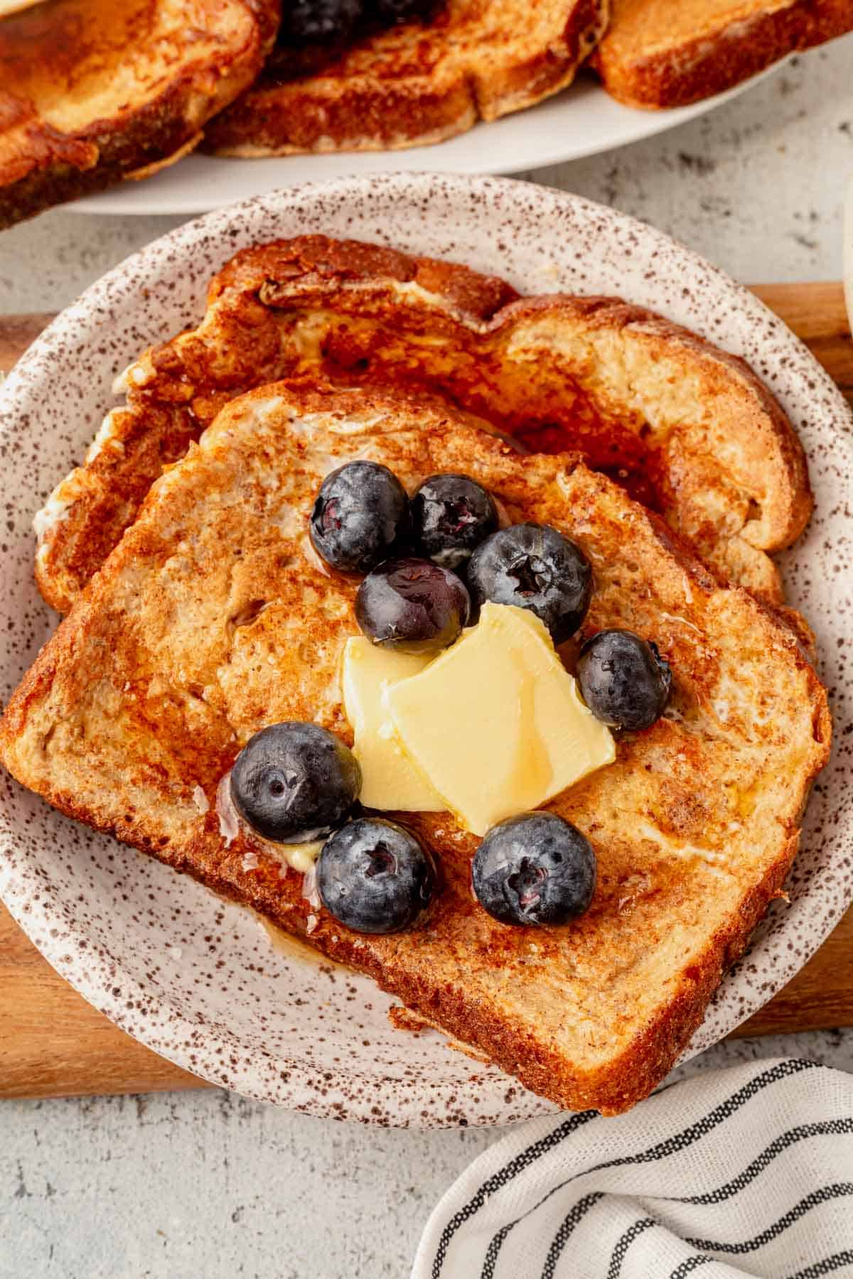 two pieces of high protein french toast on a plate with butter and blueberries.