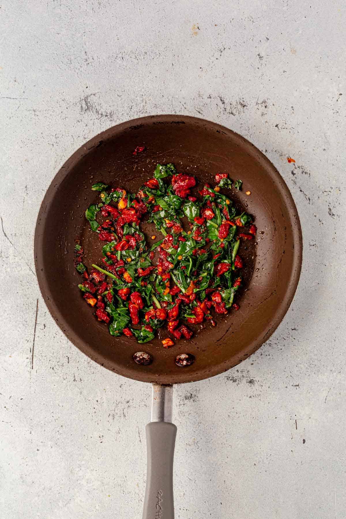 satueed spinach and sun dried tomatoes in a skillet.