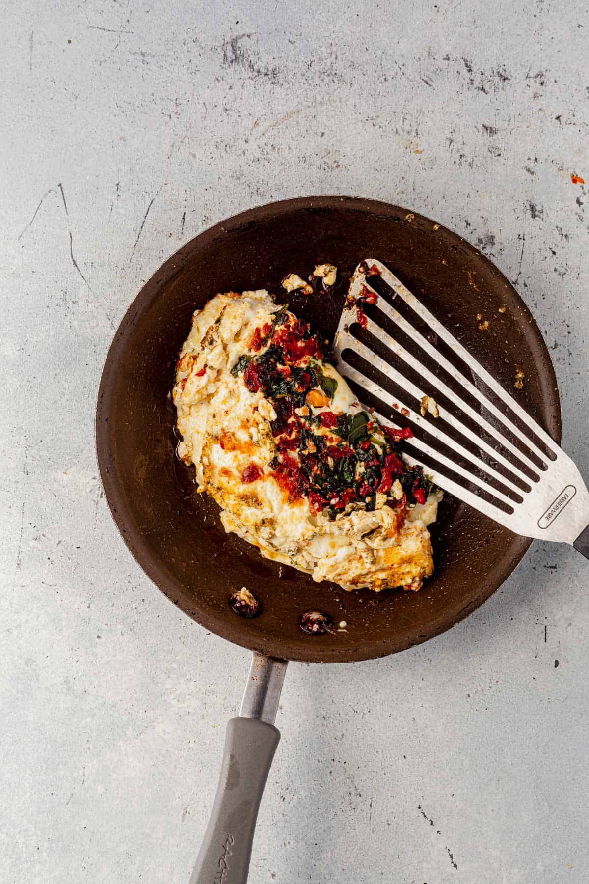 egg white, spinach, and feta omelette cooking in a pan.