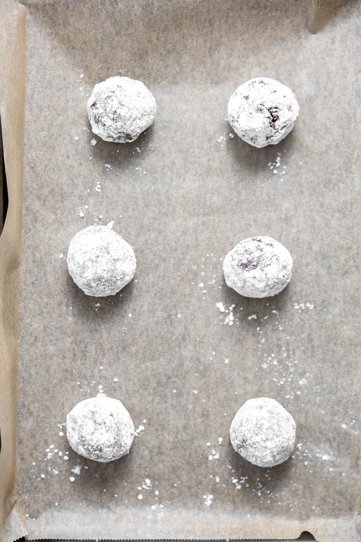 gluten free chocolate crinkle cookie dough rolled in powdered sugar on a cookie sheet.