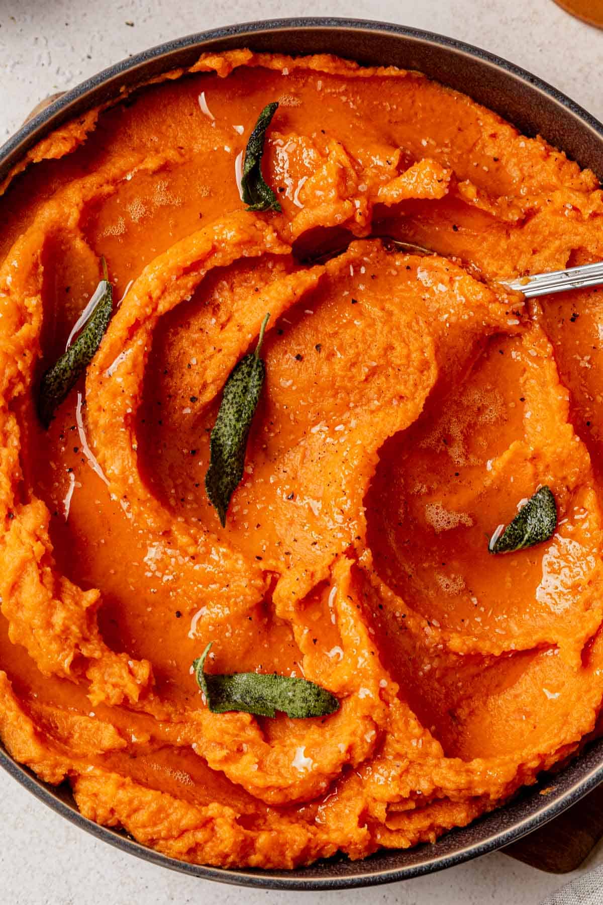 brown butter mashed sweet potatoes in a bowl with a serving spoon and crispy sage.