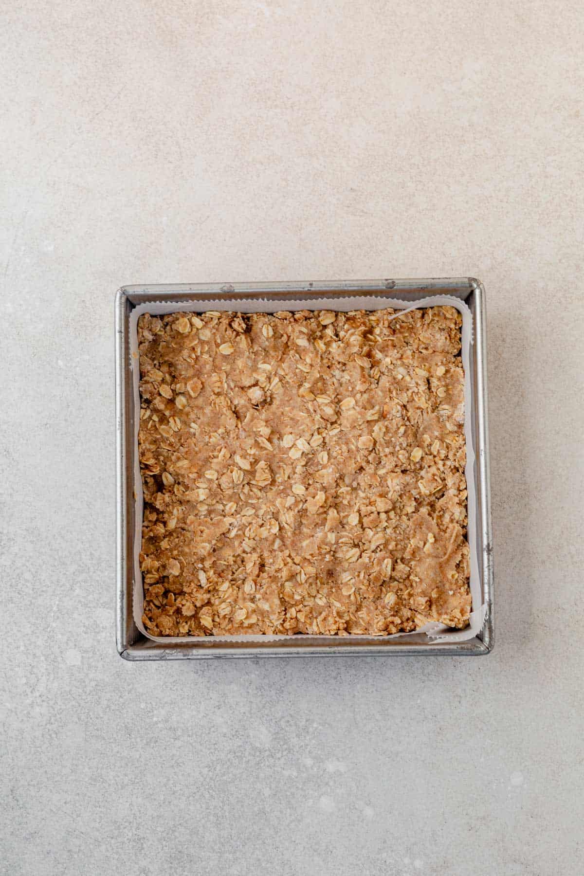 oatmeal crumb bar crust pressed into a square metal baking pan.