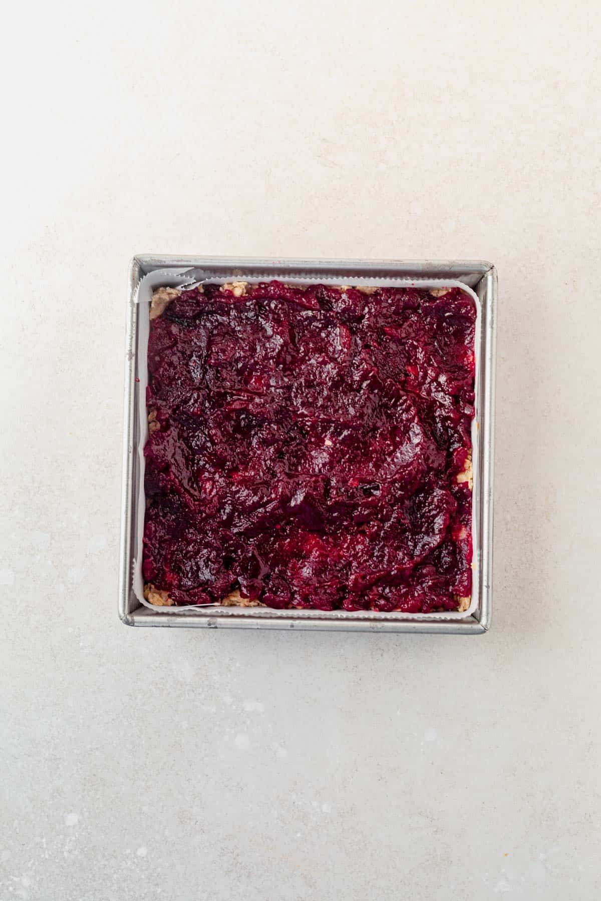 cranberry sauce spread over a layer of oatmeal crumb crust in a pan.