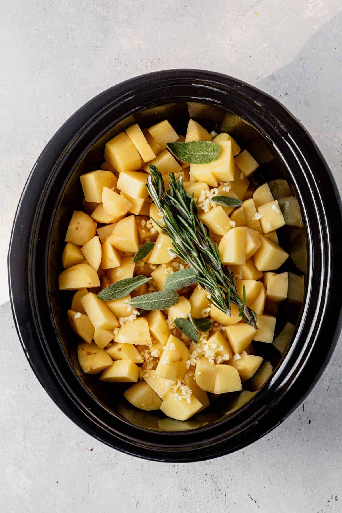 diced potatoes in a crock pot with fresh herbs on top.