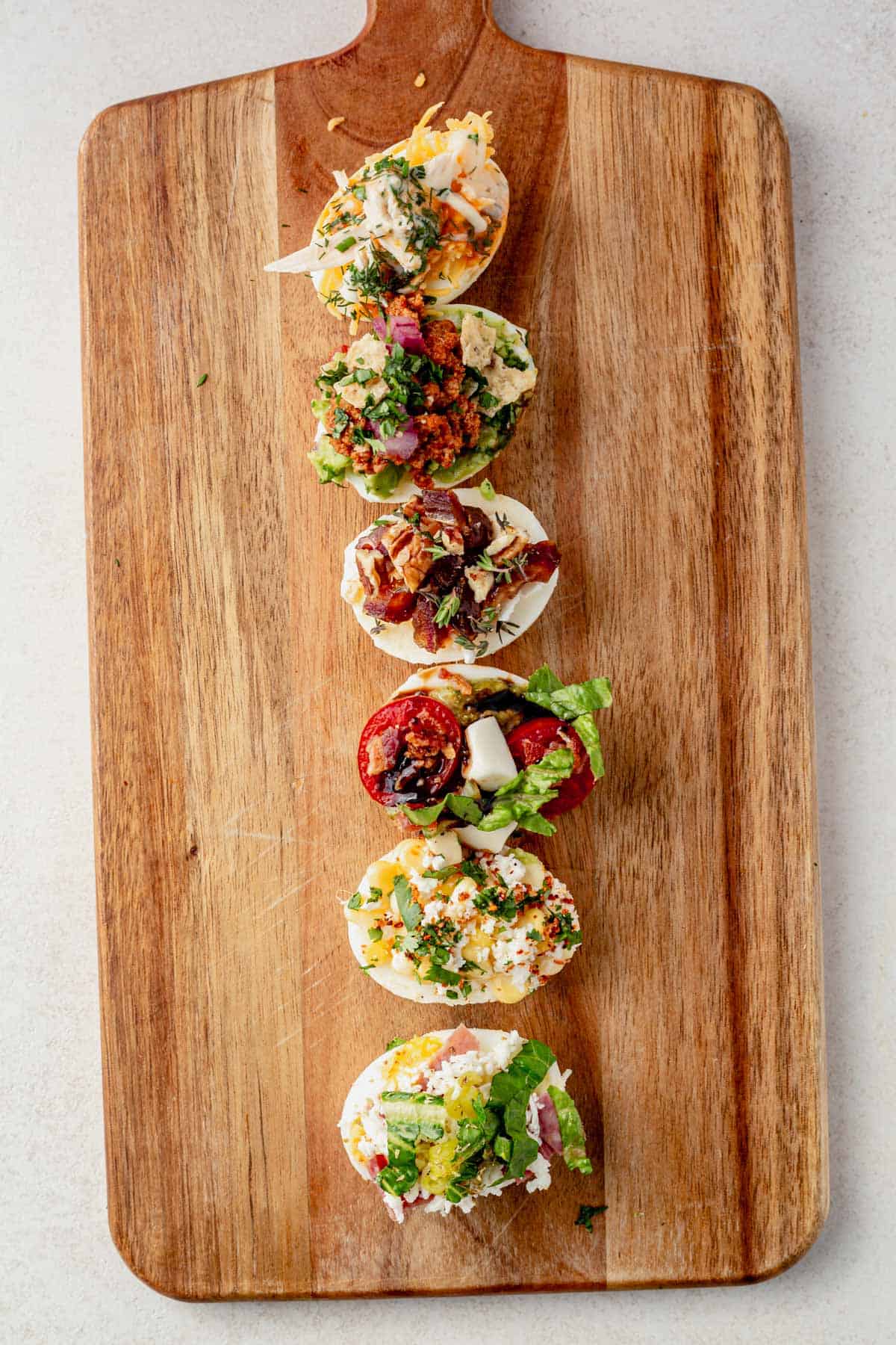 egg flight on a cutting board with different toppings on 6 hard boiled eggs.