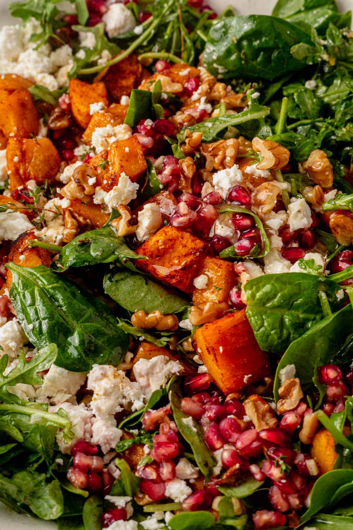 pumpkin and feta salad tossed with pomegranate and spinach in a bowl.