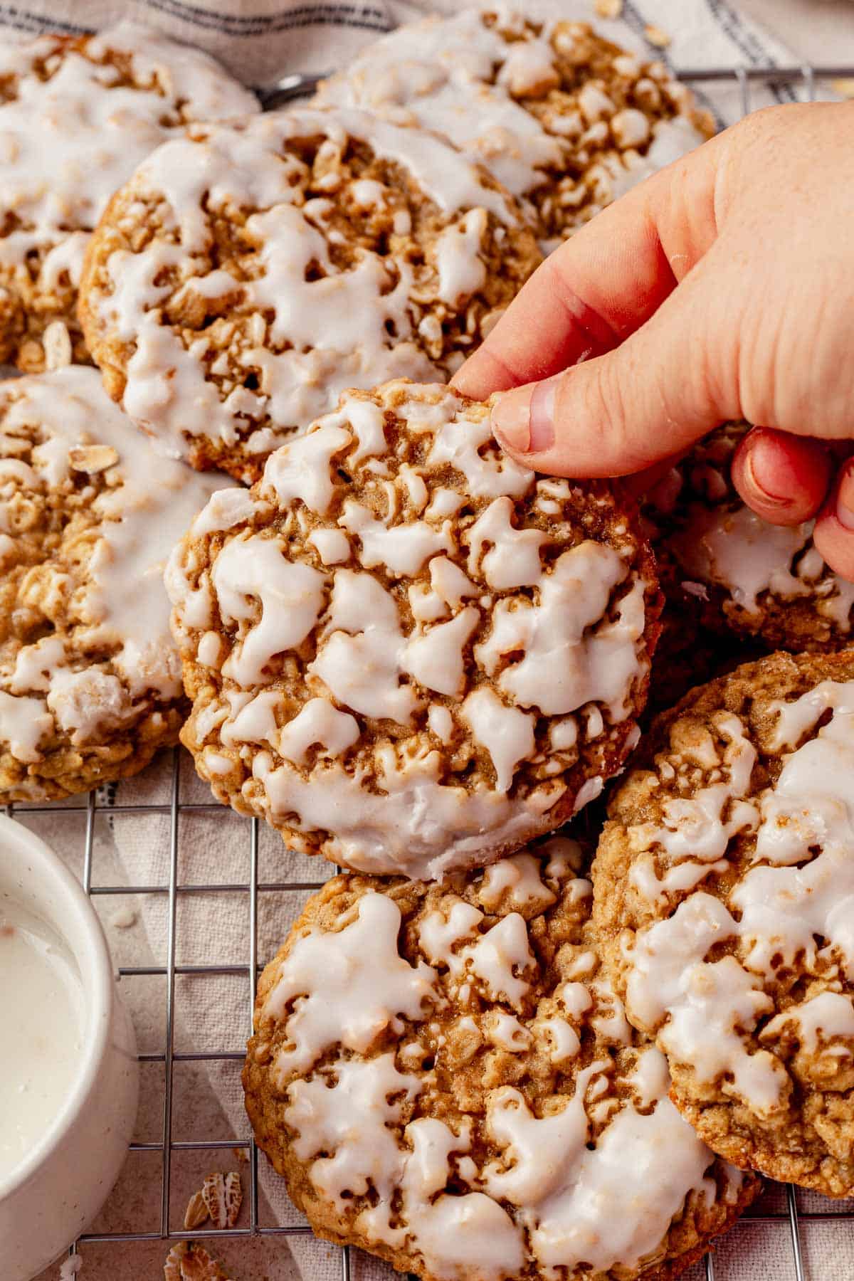 picking up an iced oatmeal cookie from a cooling rack.