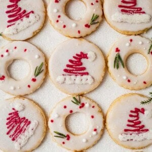 shortbread cutout cookies decorated with santa hats and wreaths on a table.