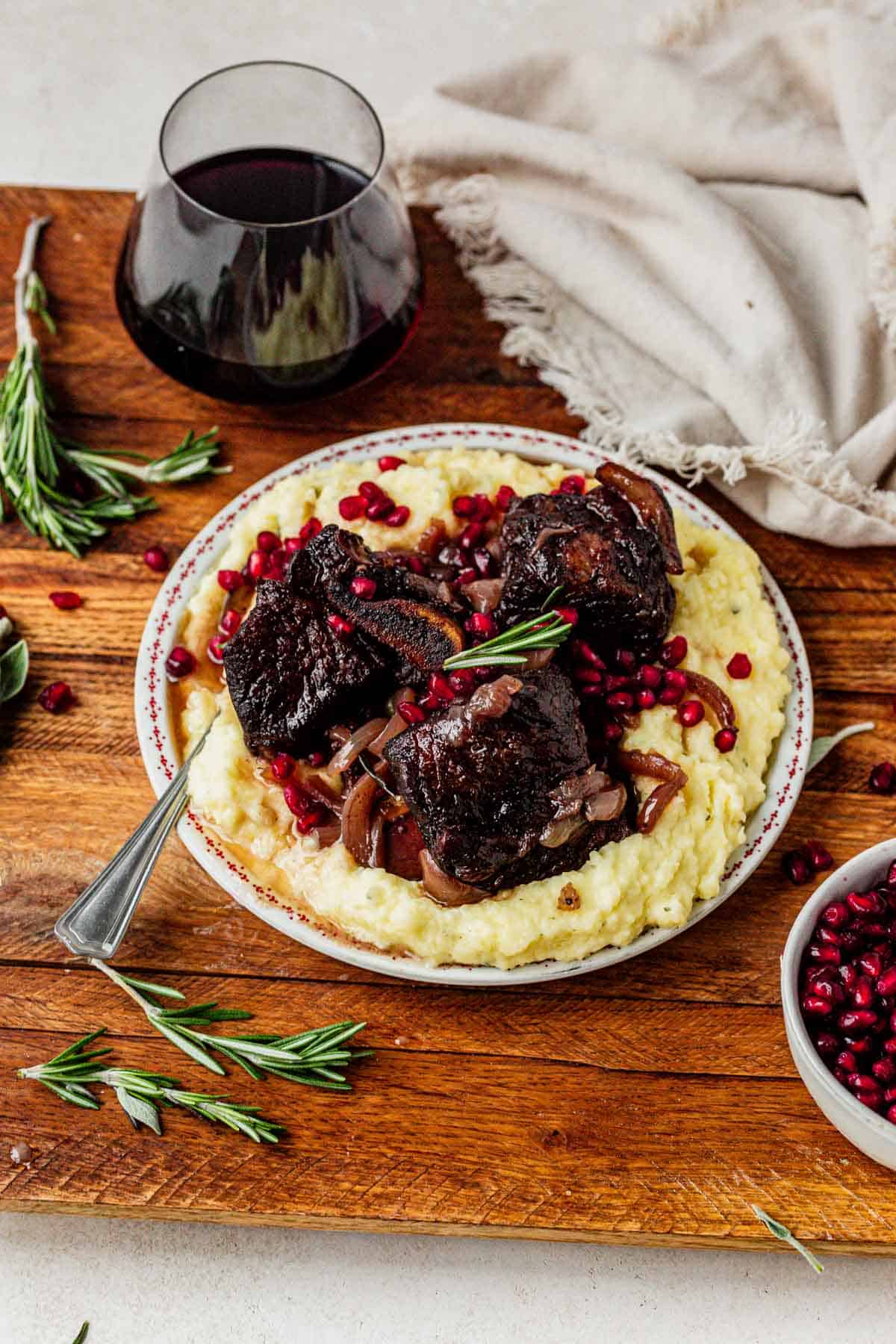 a plate of mashed potatoes and pomegranate short ribs with a glass of red wine.