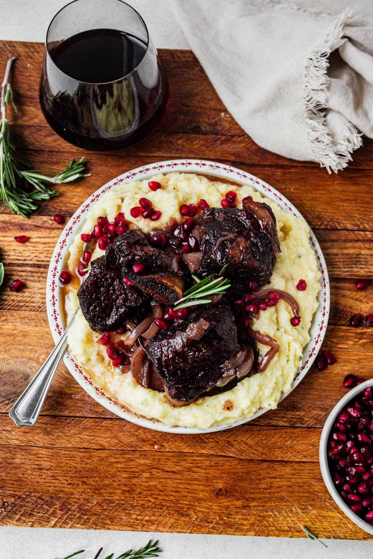 pomegranate short ribs on a plate of mashed potatoes with pomegranate arils on top.