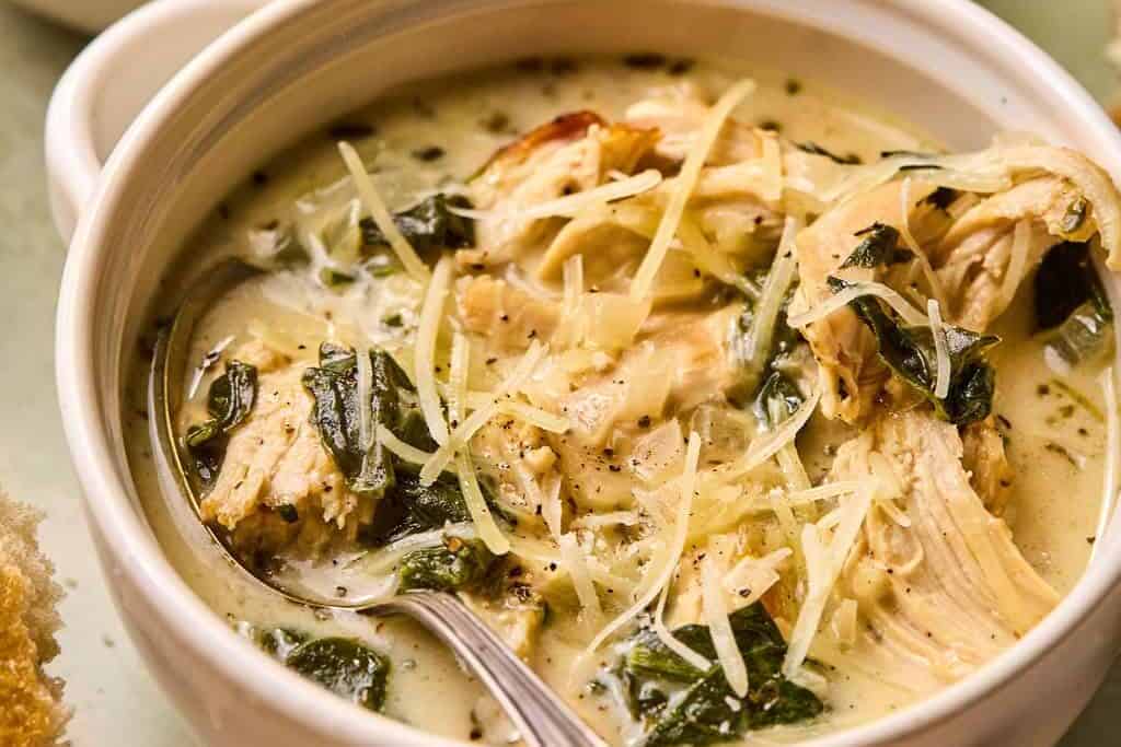 two bowls of chicken florentine soup with a spoon in it.