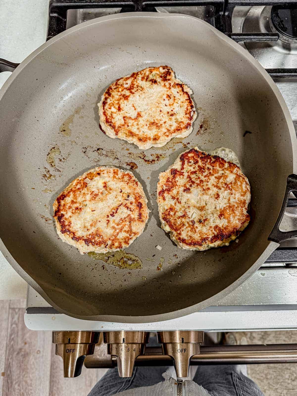 cooking chicken feta burgers in a skillet on the stove.