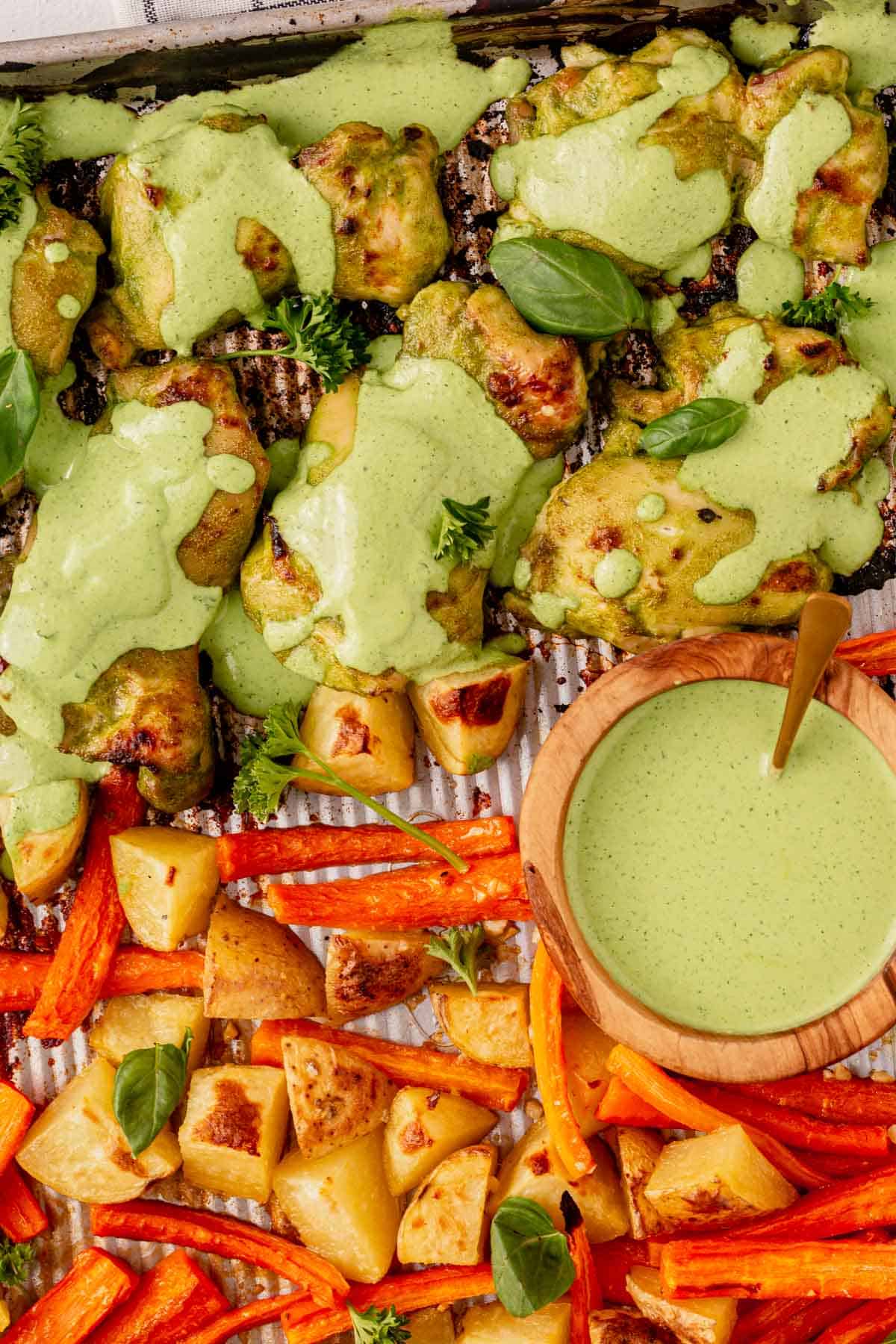 green goddess sauce spooned over green goddess chicken on a sheet pan.