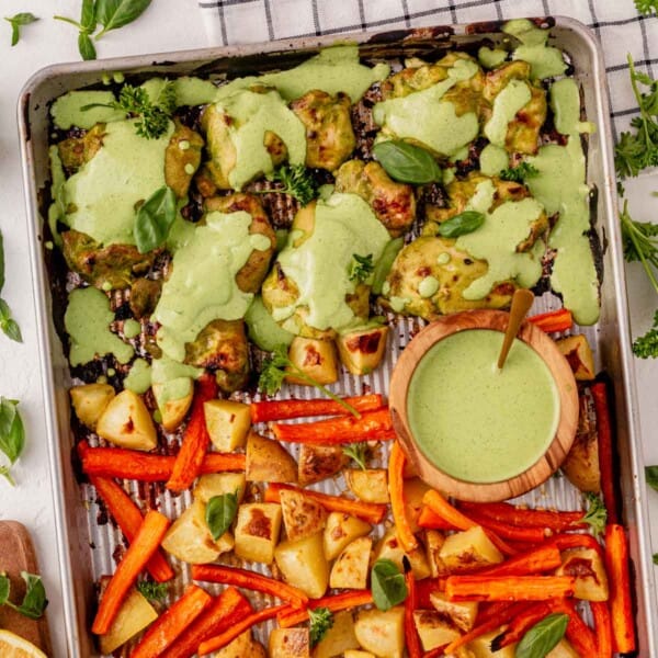 green goddess chicken on a sheet pan with veggies and extra green goddess sauce.