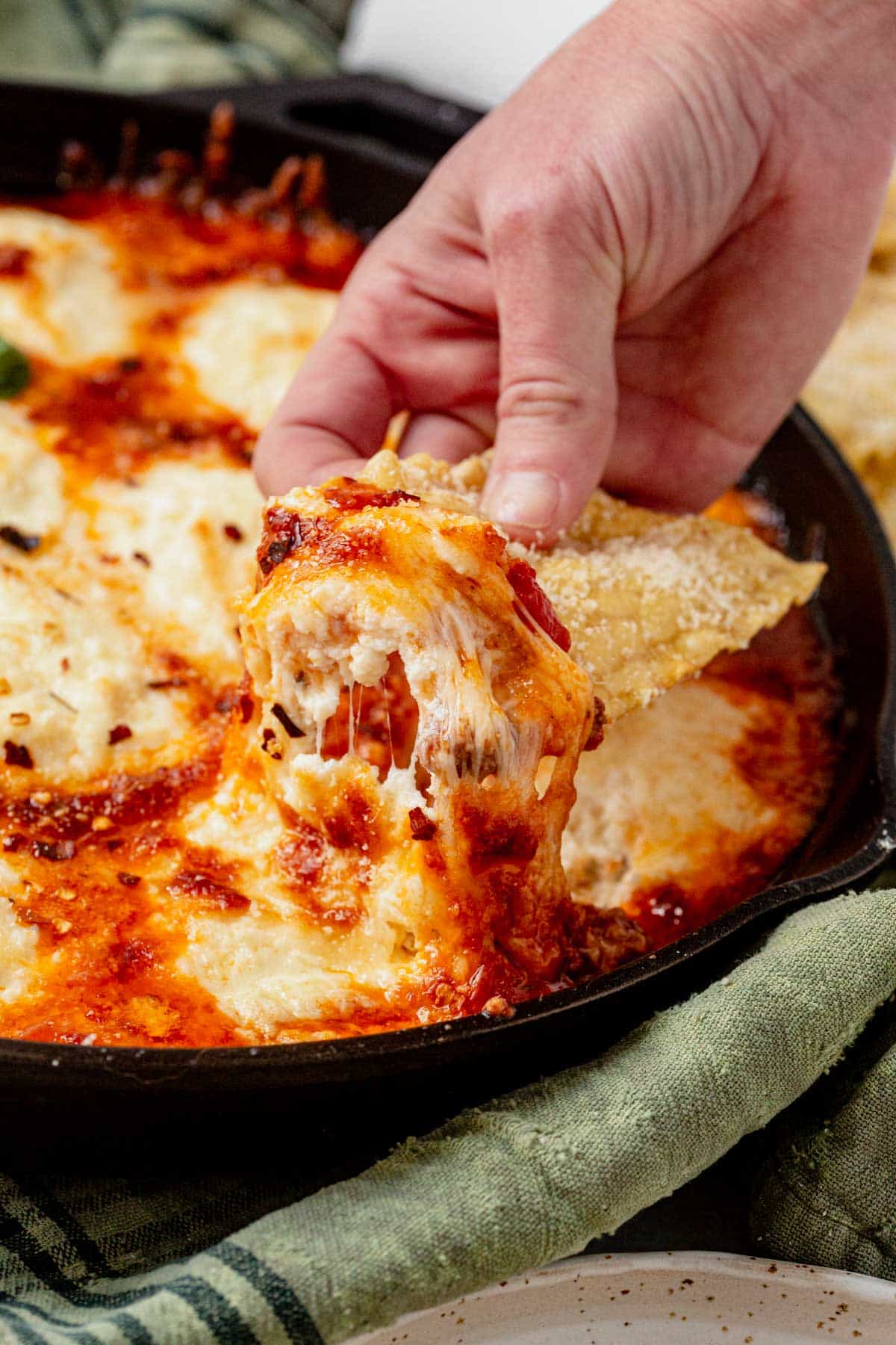 scooping lasagna dip from a skillet.