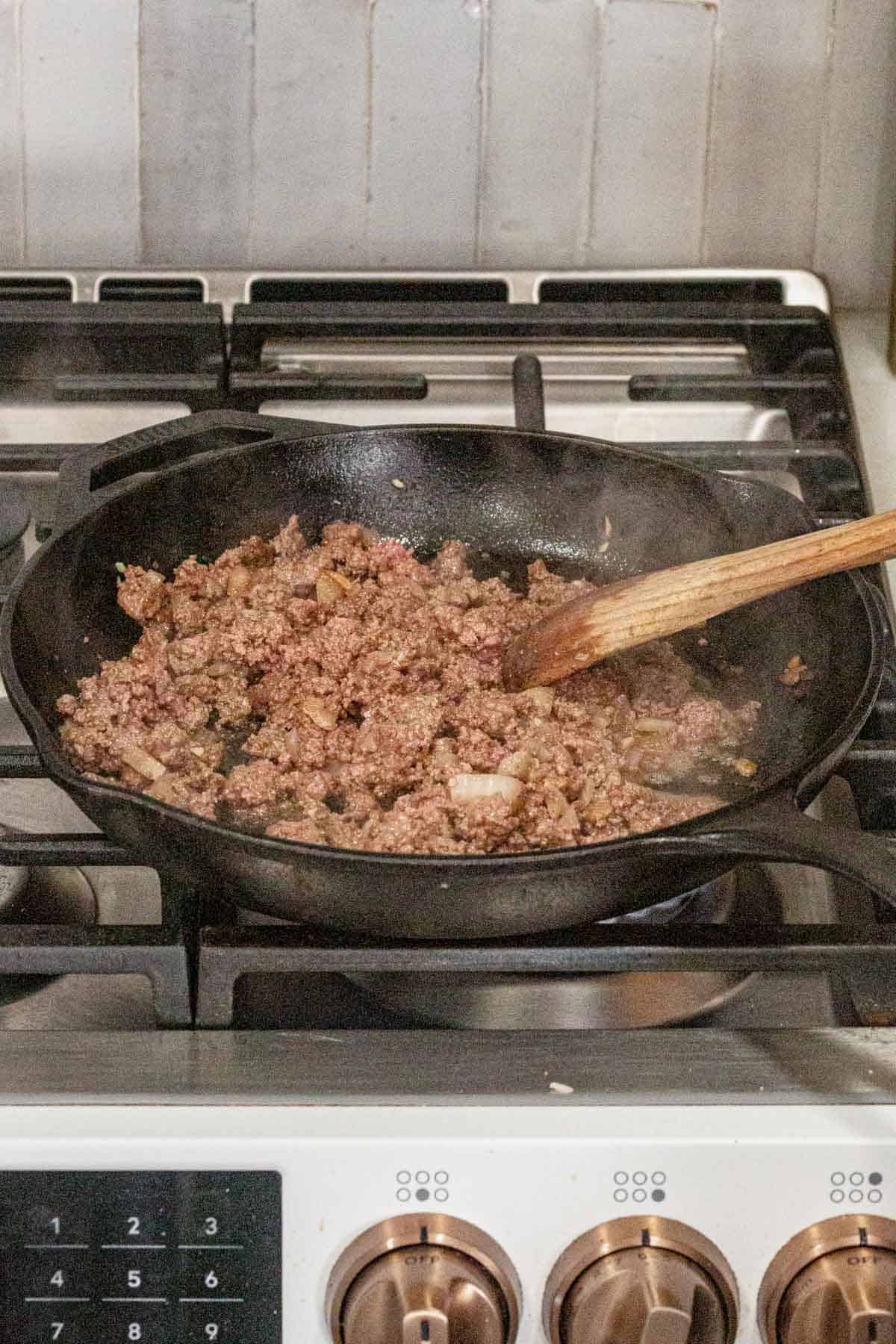 browned beef, onions, and garlic cooking on the stove.