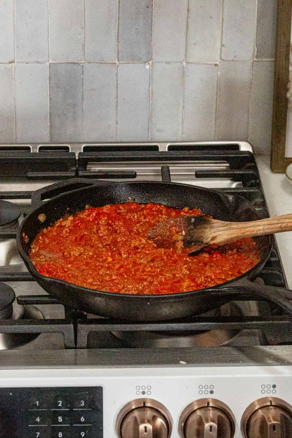 Stirring marinara sauce into a cast iron skillet with browned beef.