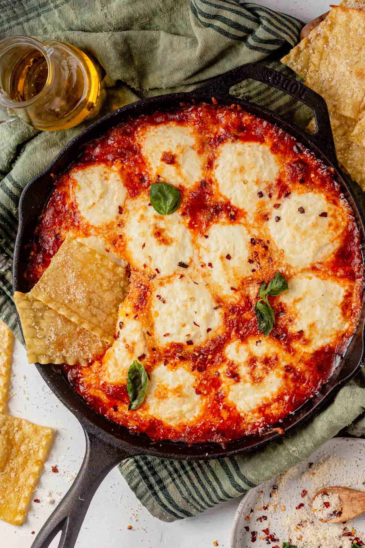 lasagna dip in a cast iron skillet with pasta chips and basil.