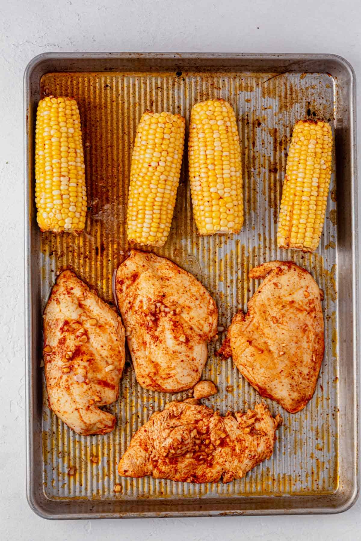 baked chicken and corn on a sheet pan.