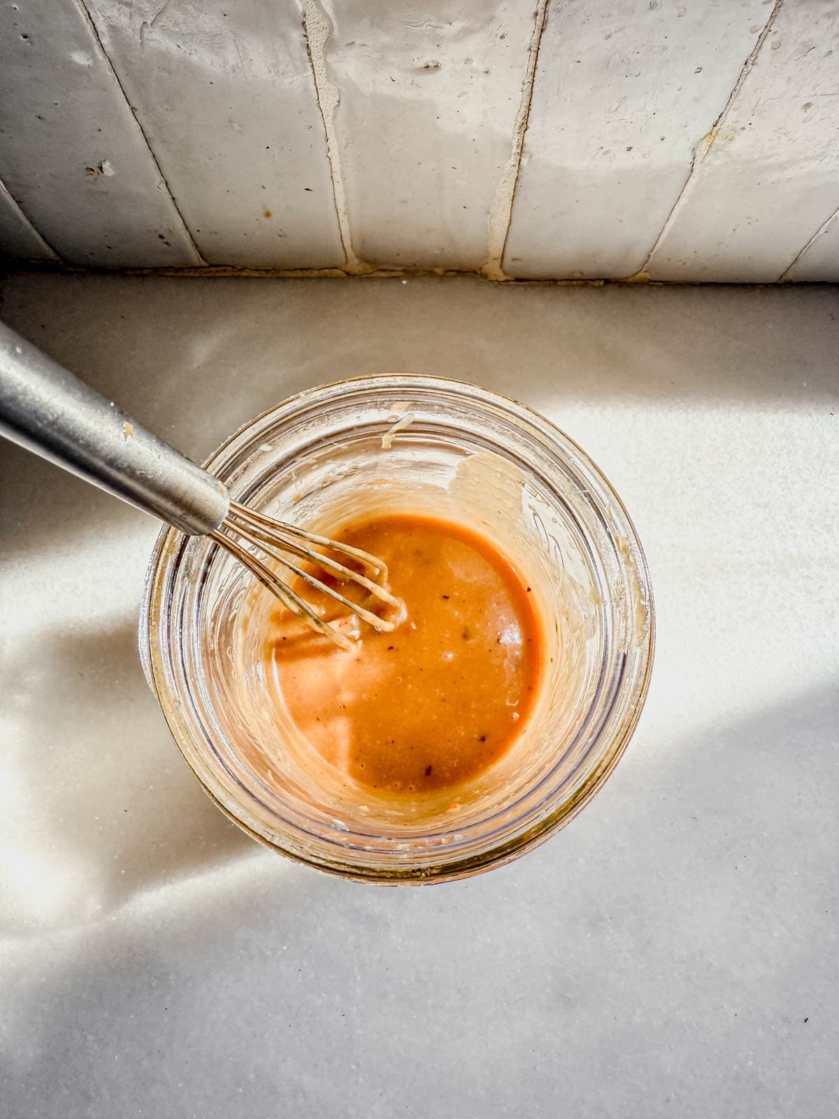 tahini ginger salad dressing in a jar with a whisk.