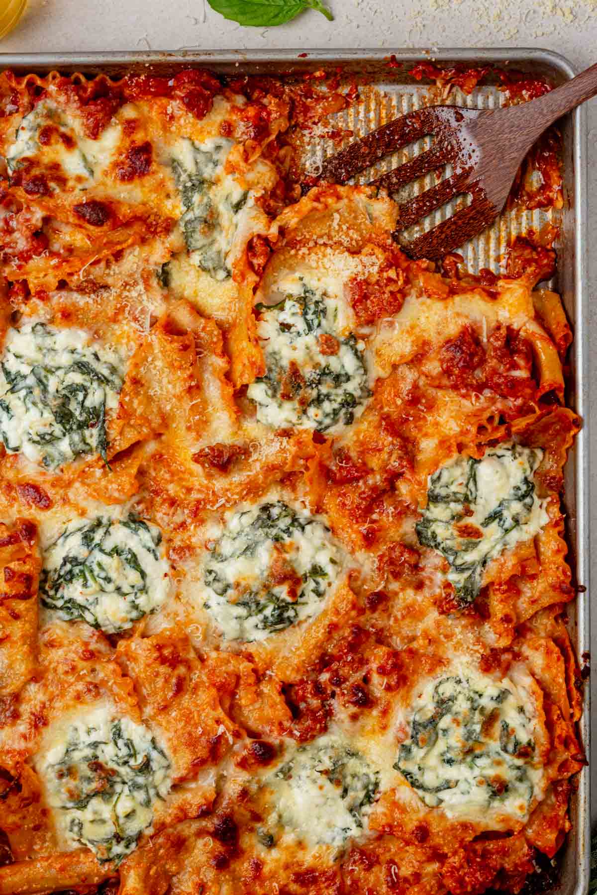 scooping a piece of sheet pan lasagna from a baking sheet.