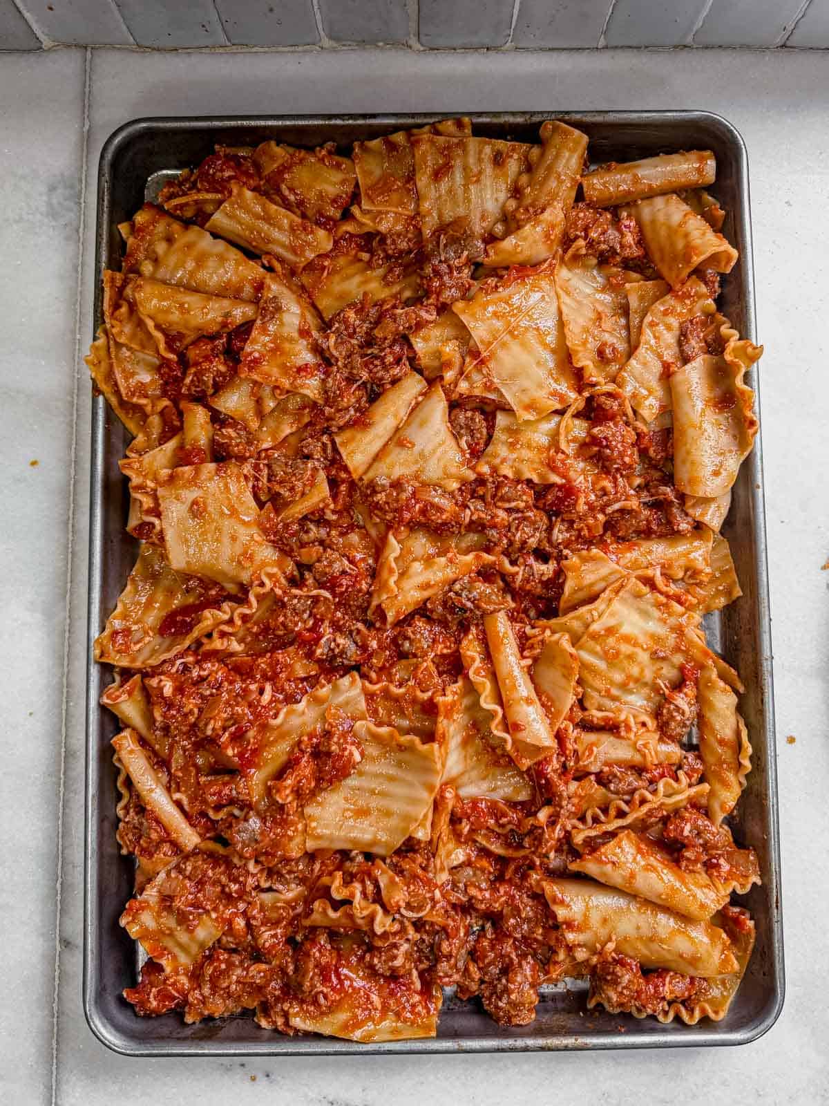 cooked lasagna noodles and meat sauce spread on a sheet pan.