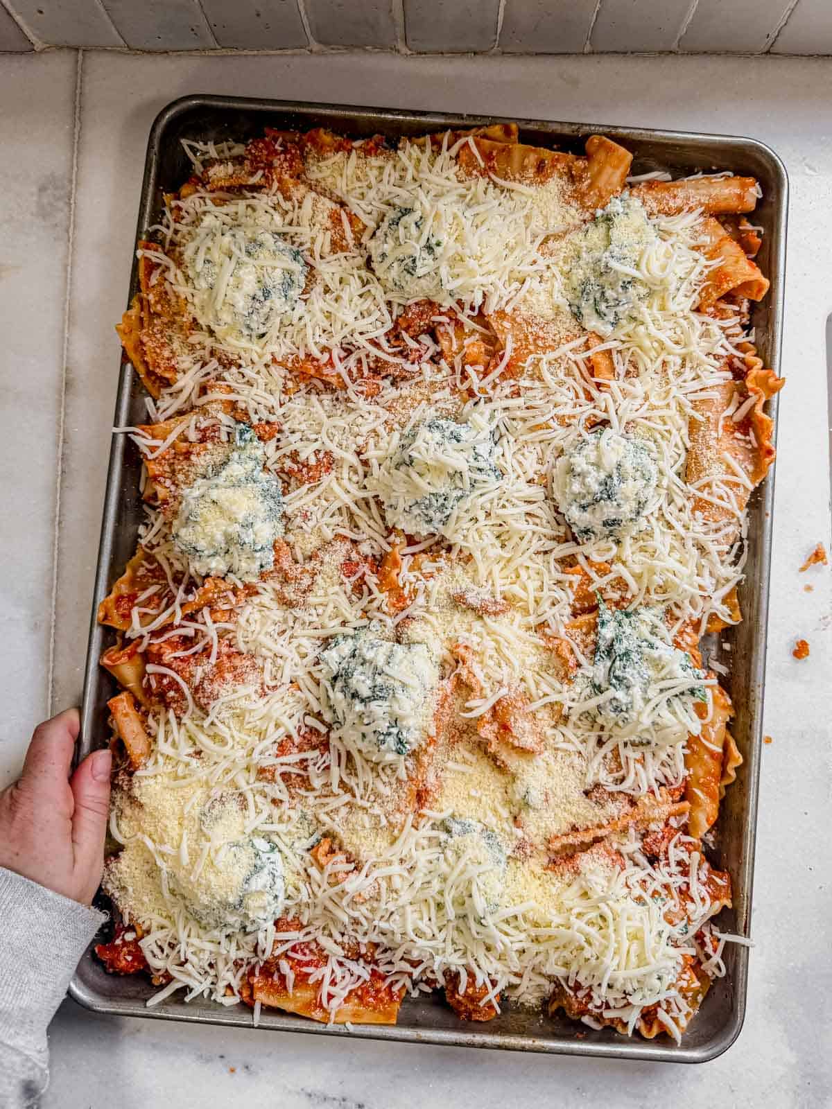 sheet pan lasagna topped with spoonfuls of ricotta and shredded cheese.