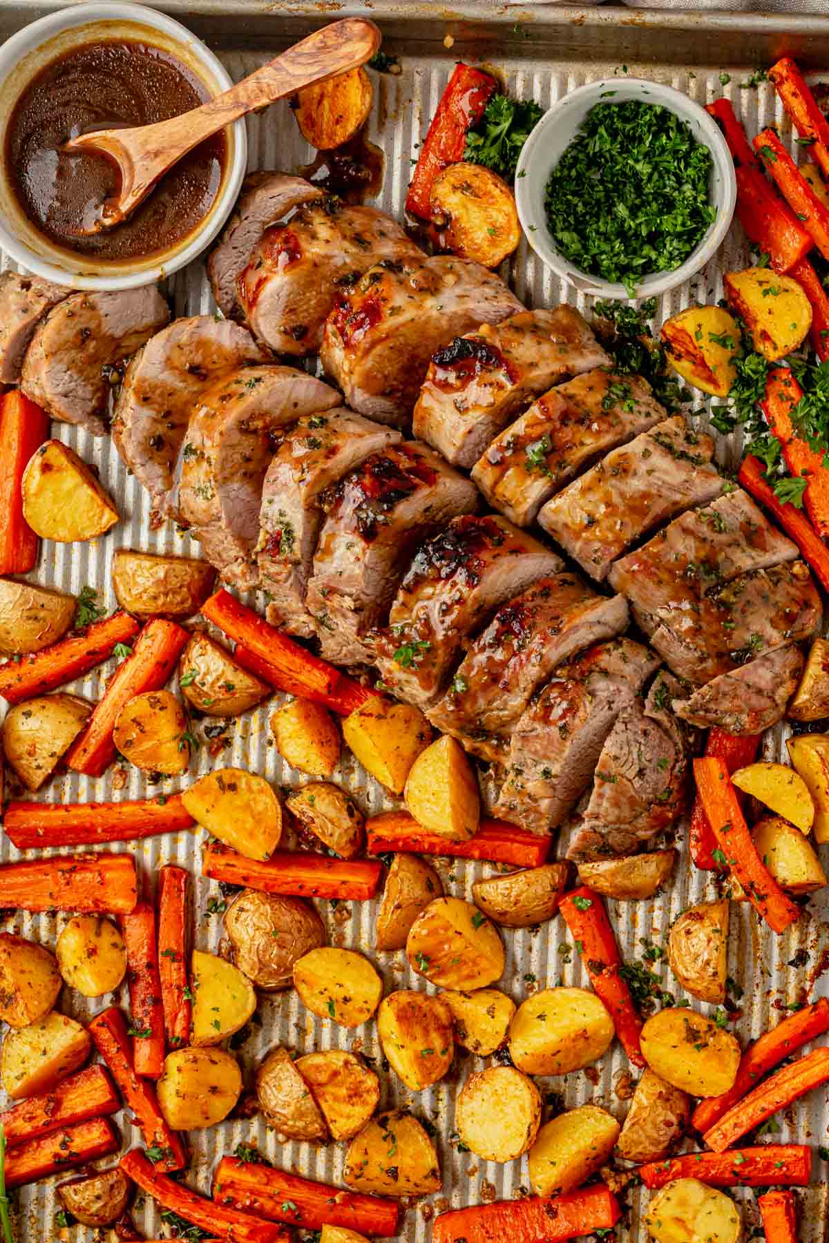 sheet pan pork tenderloin with potatoes and carrots topped with a glaze and fresh parsley.