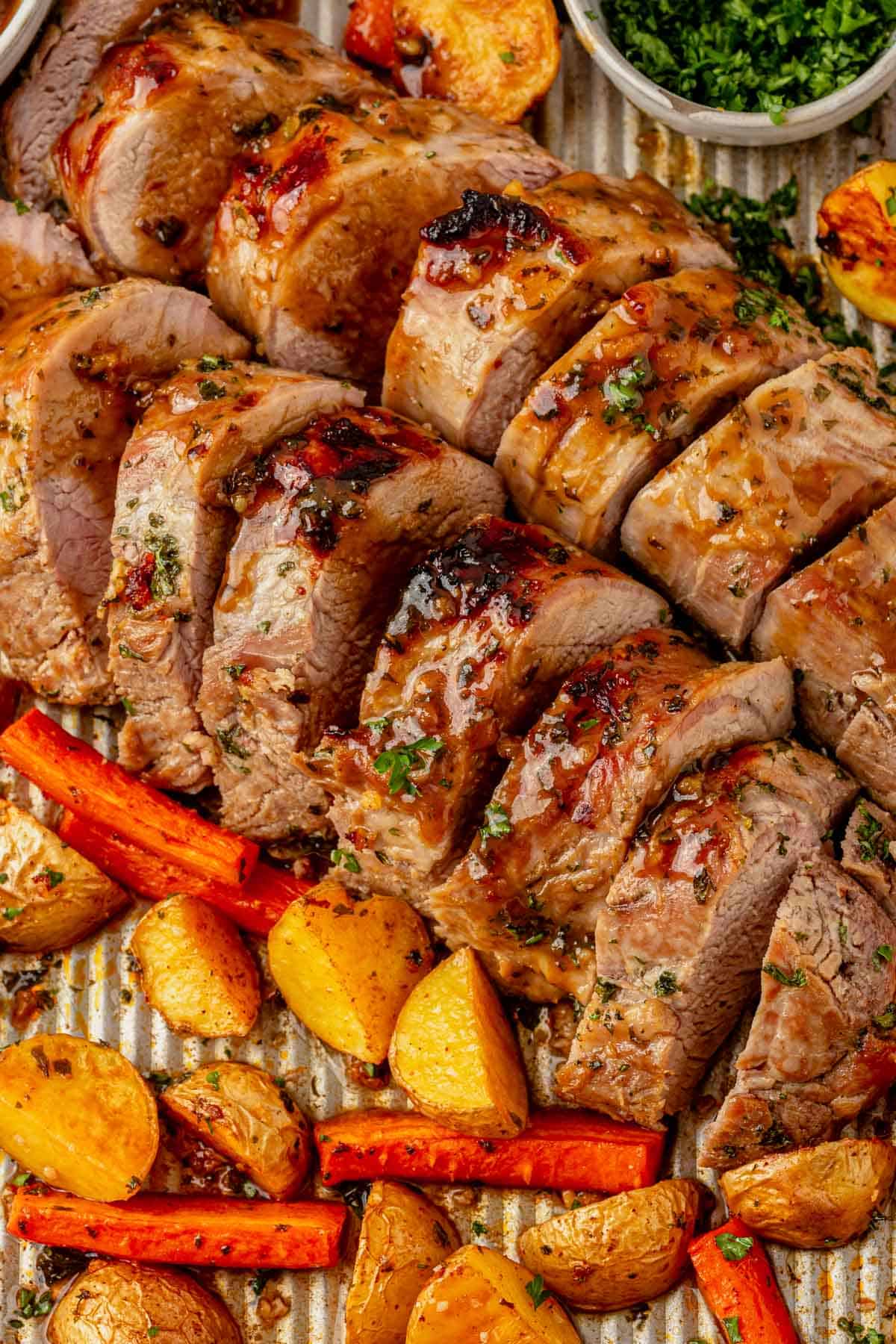 sliced pork tenderloin on a sheet pan with roasted vegetables.