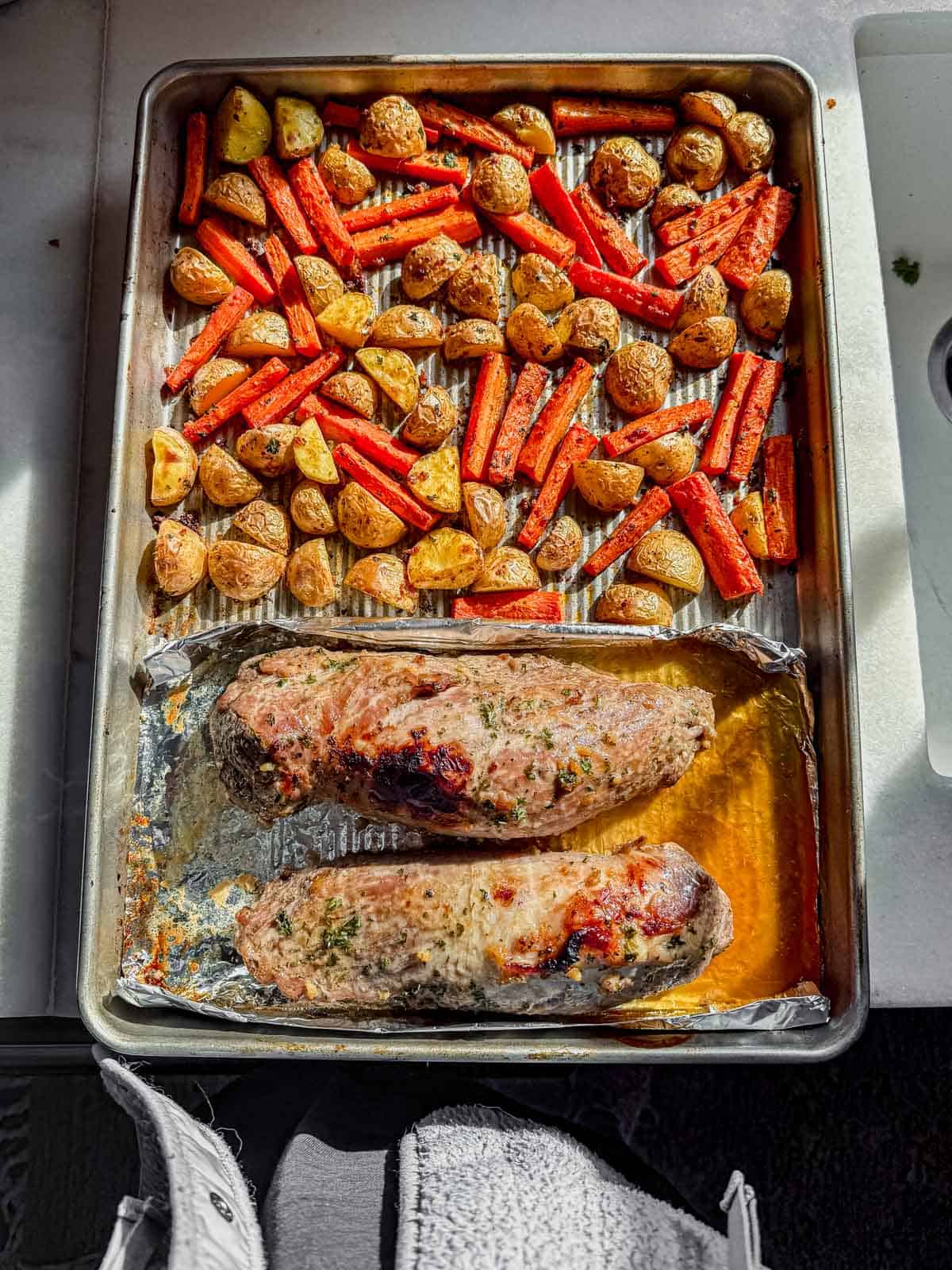 roasted pork tenderlion and vegetables resting on a sheet pan.