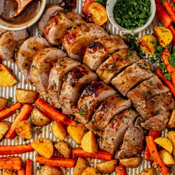 pork tenderloin sliced on a sheet pan with roasted carrots and vegetables.