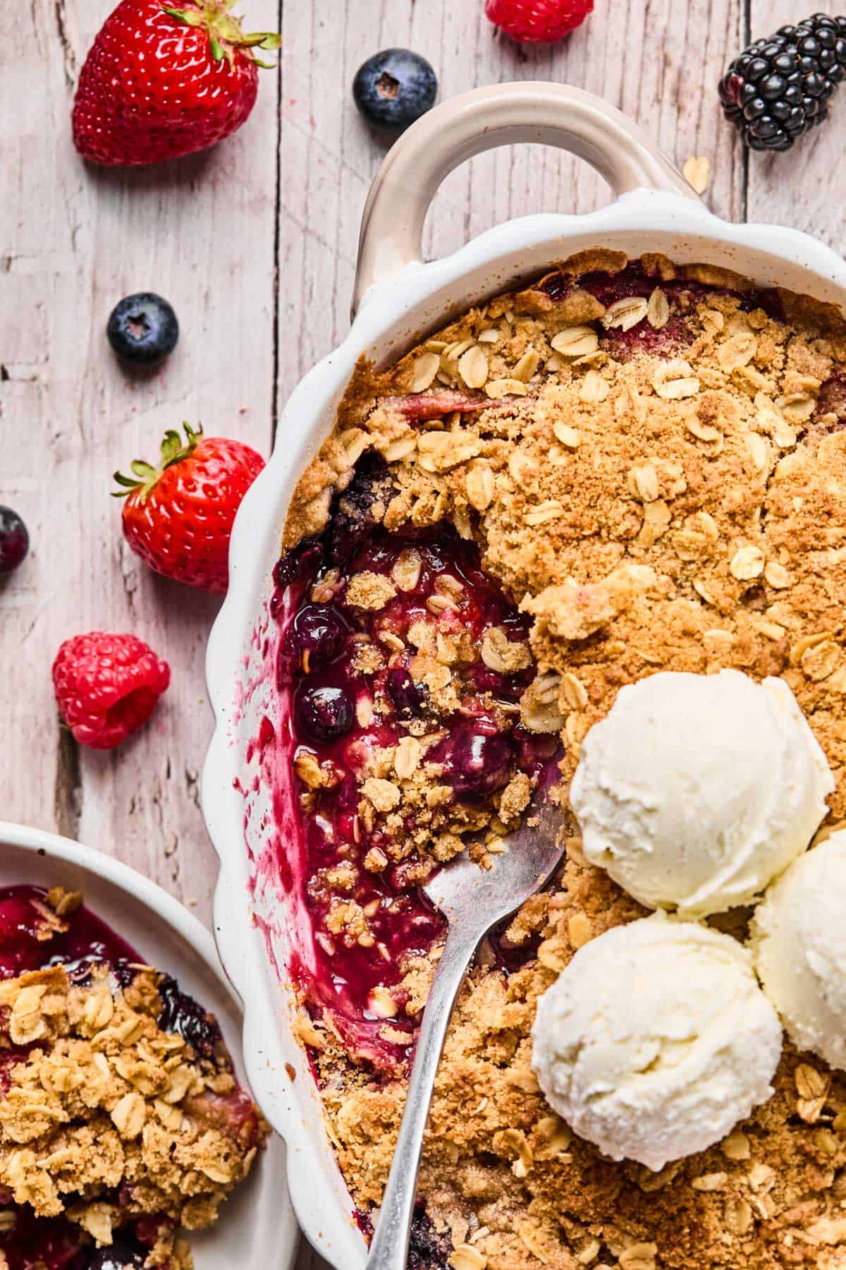 spoon scooped into gluten free berry crisp with two scoops of vanilla ice cream on top