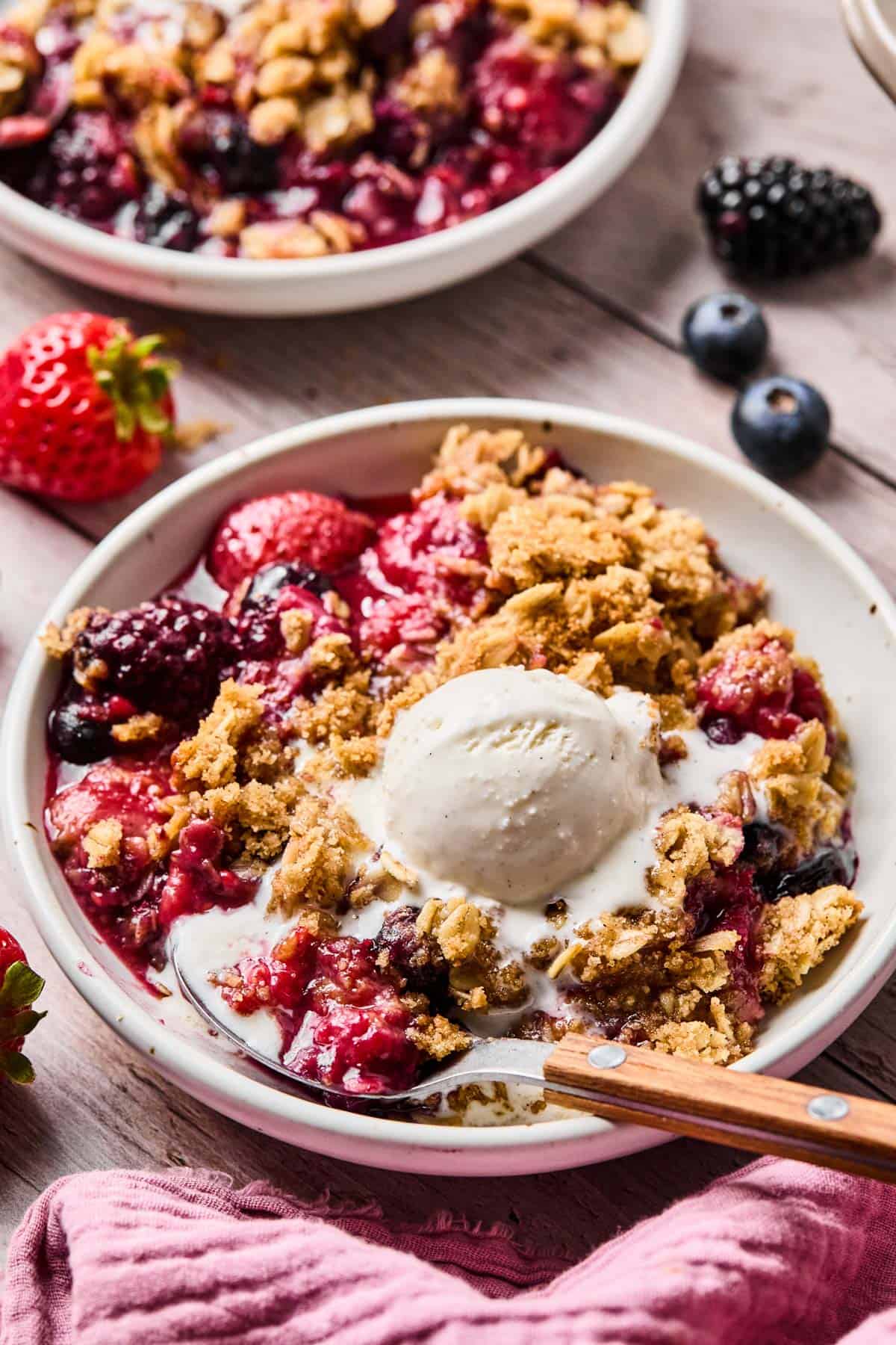 spoon in a bowl with a serving of gluten free berry crisp and a scoop of vanilla ice cream on top