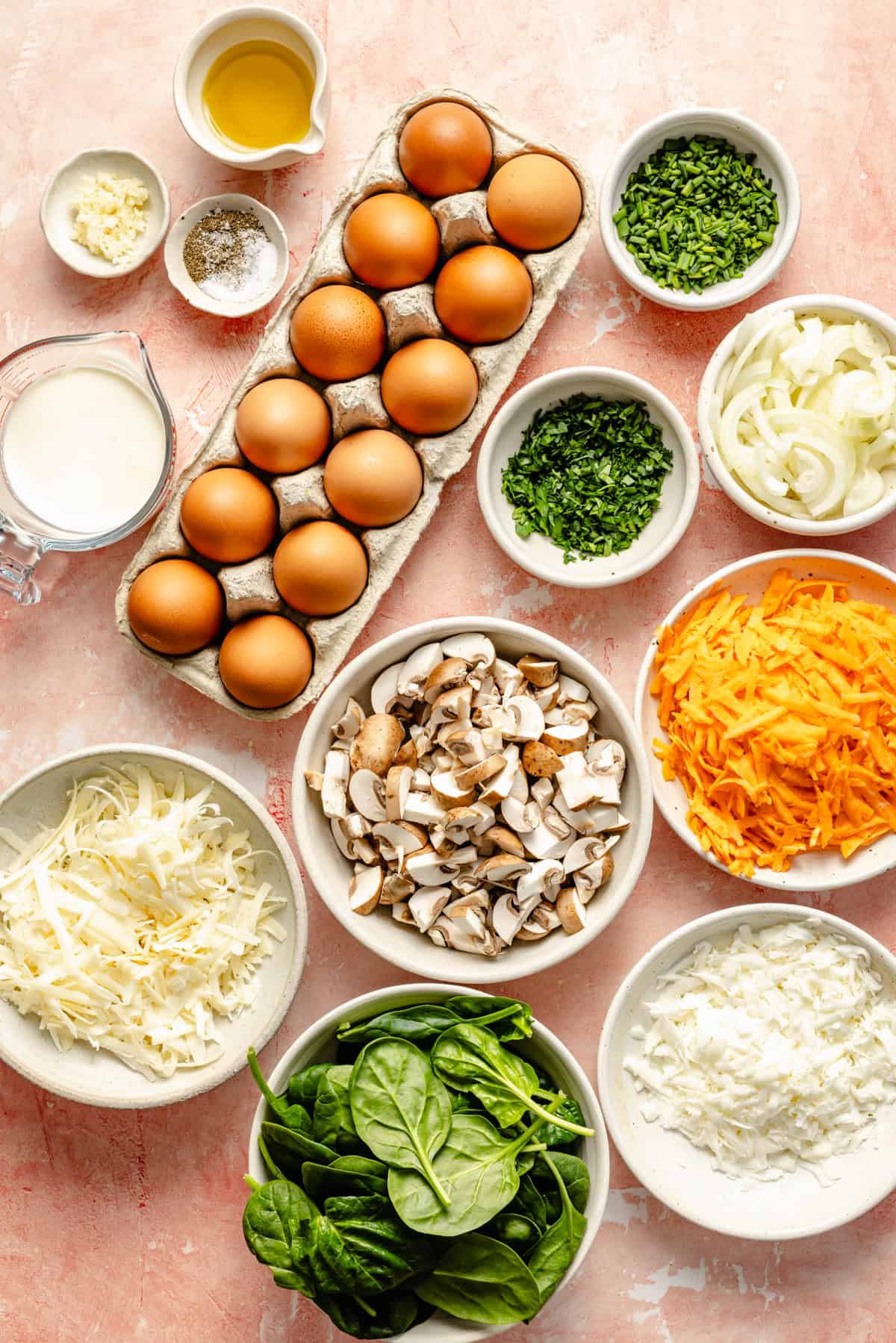 ingredients to make a vegetable frittata separated into white bowls on a marble countertop