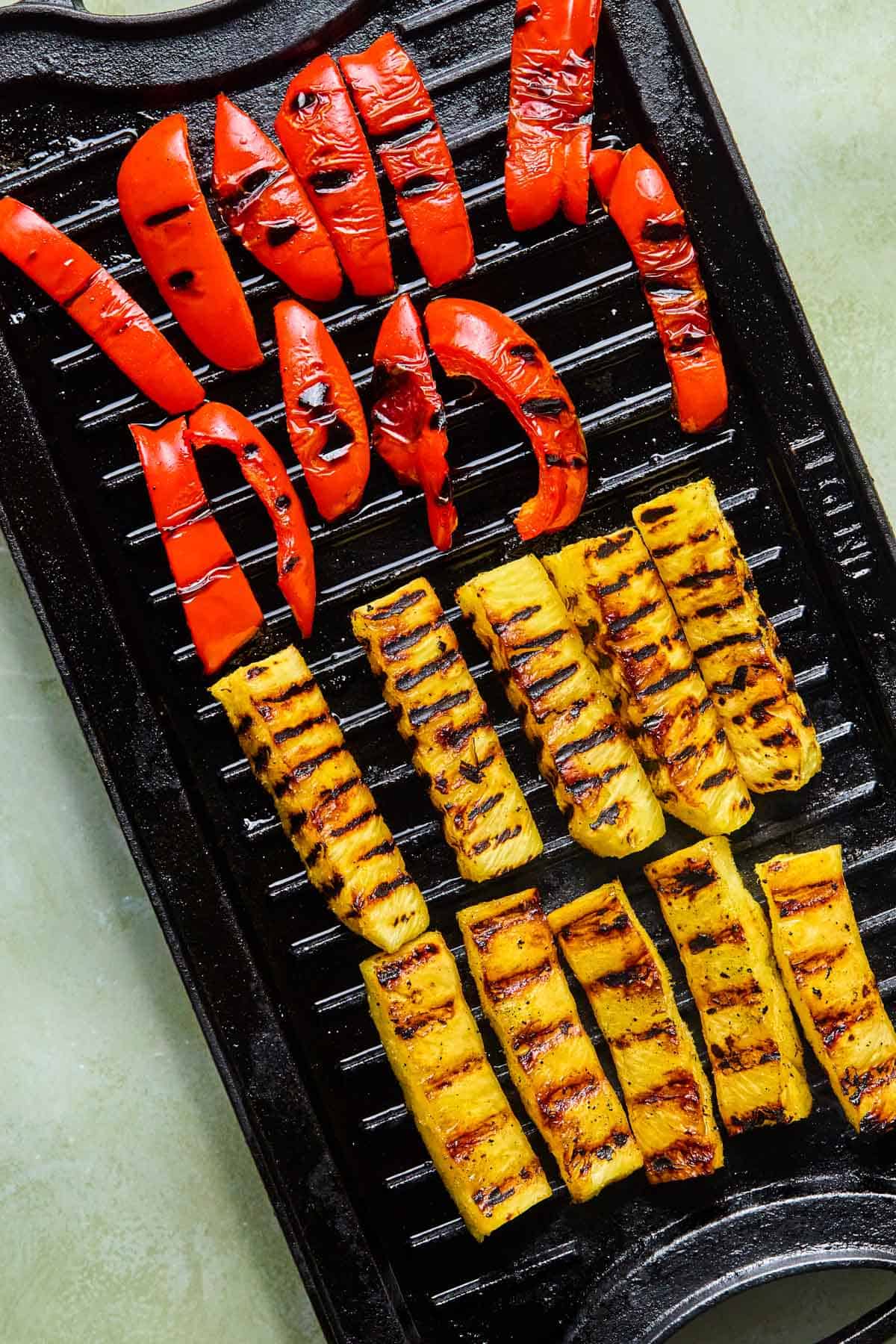 grilling pineapple spears and sliced red pepper on a grill.