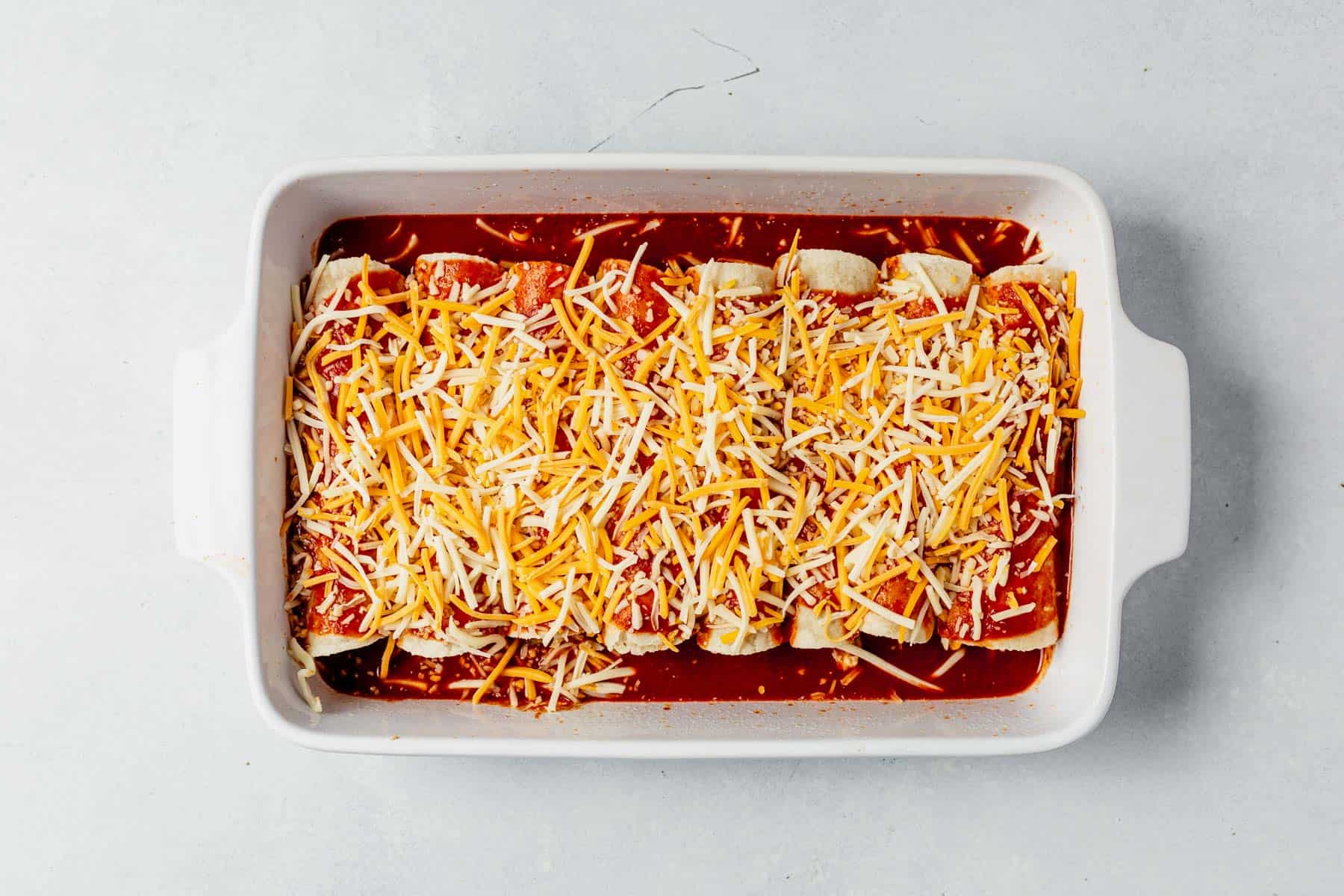 healthy chicken enchiladas assembled and lined up in a 9x13 before baking