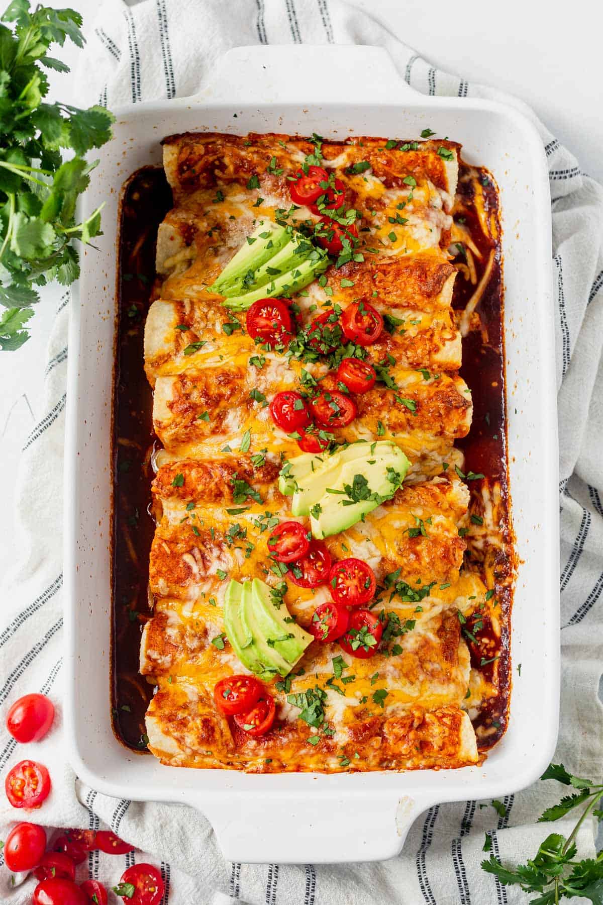 healthy chicken enchiladas baked in a 9x13 and topped with sliced cherry tomatoes and sliced avocado