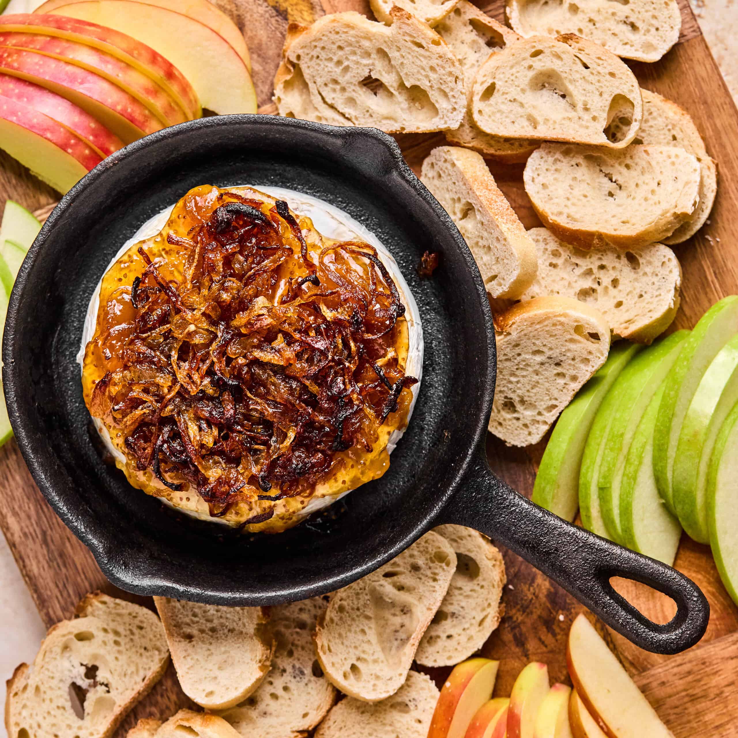 baked brie with fig jam and caramelized onion in a cast iron skillet with baguette slices and apple slices