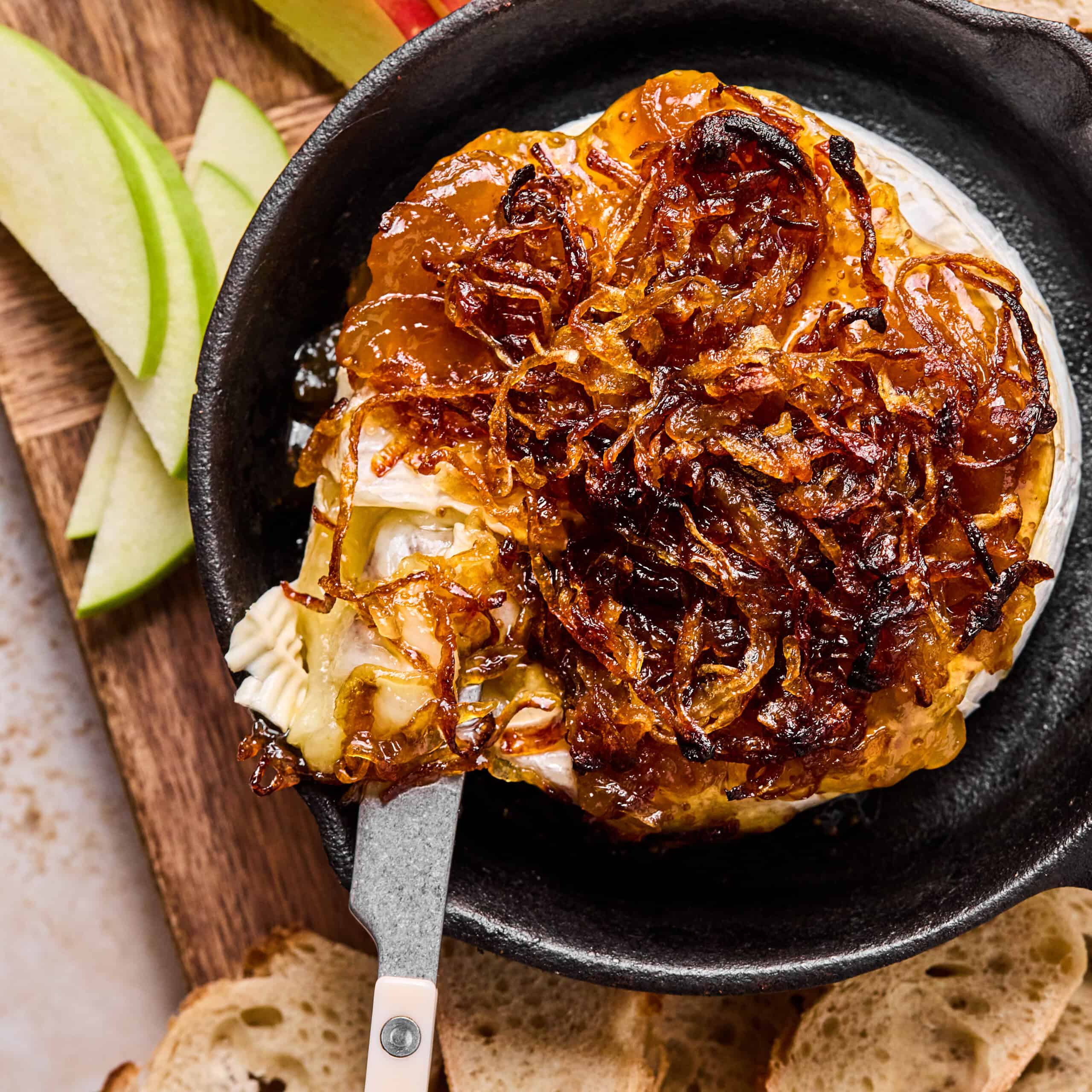 baked brie with fig jam and caramelized onion in a cast iron wtih a knife cutting into it