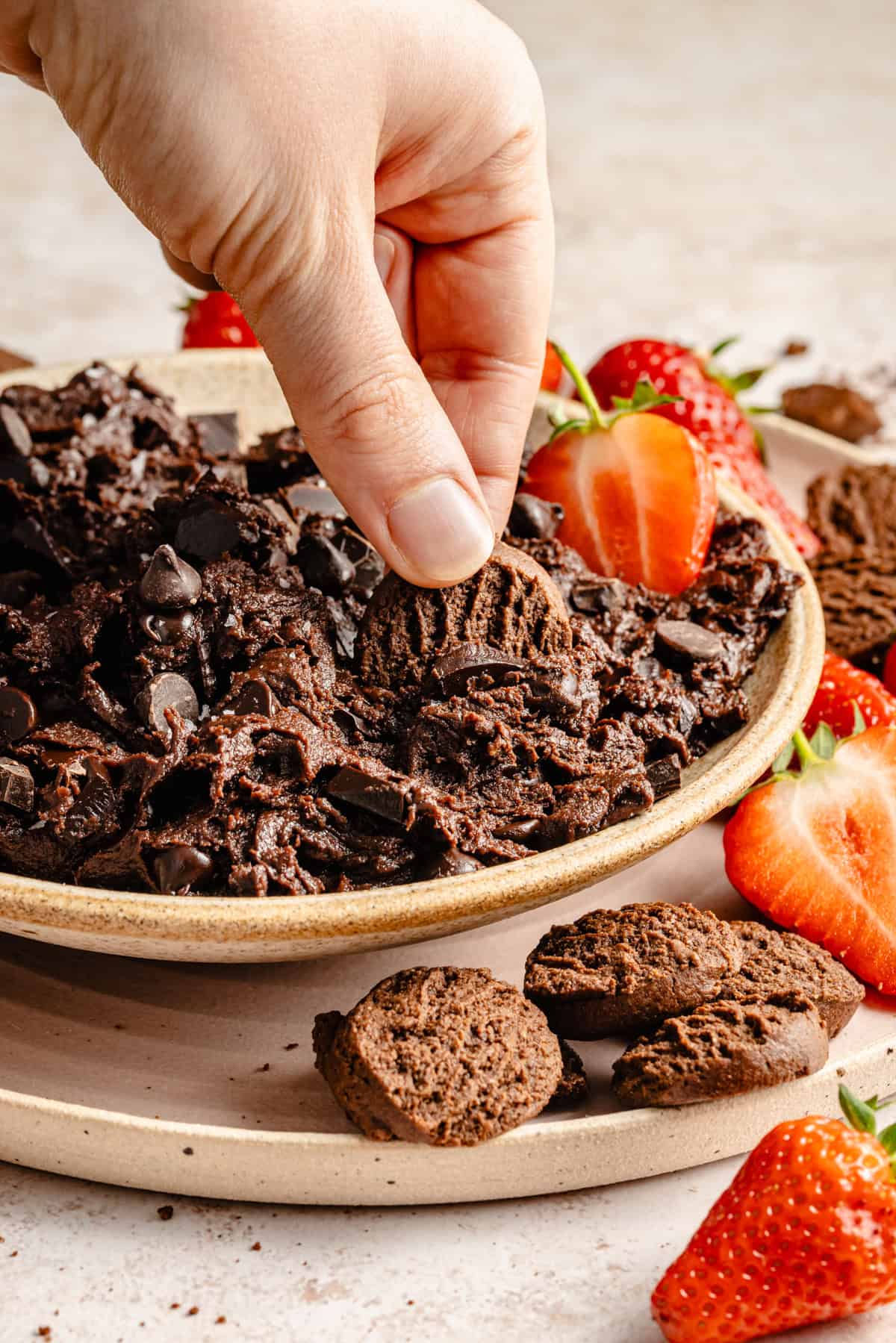 hand dipping into edible brownie batter with strawberry slices
